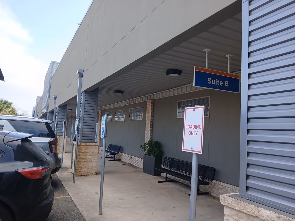 Exterior corridor of a facility with benches, a Suite B sign, and parked cars.