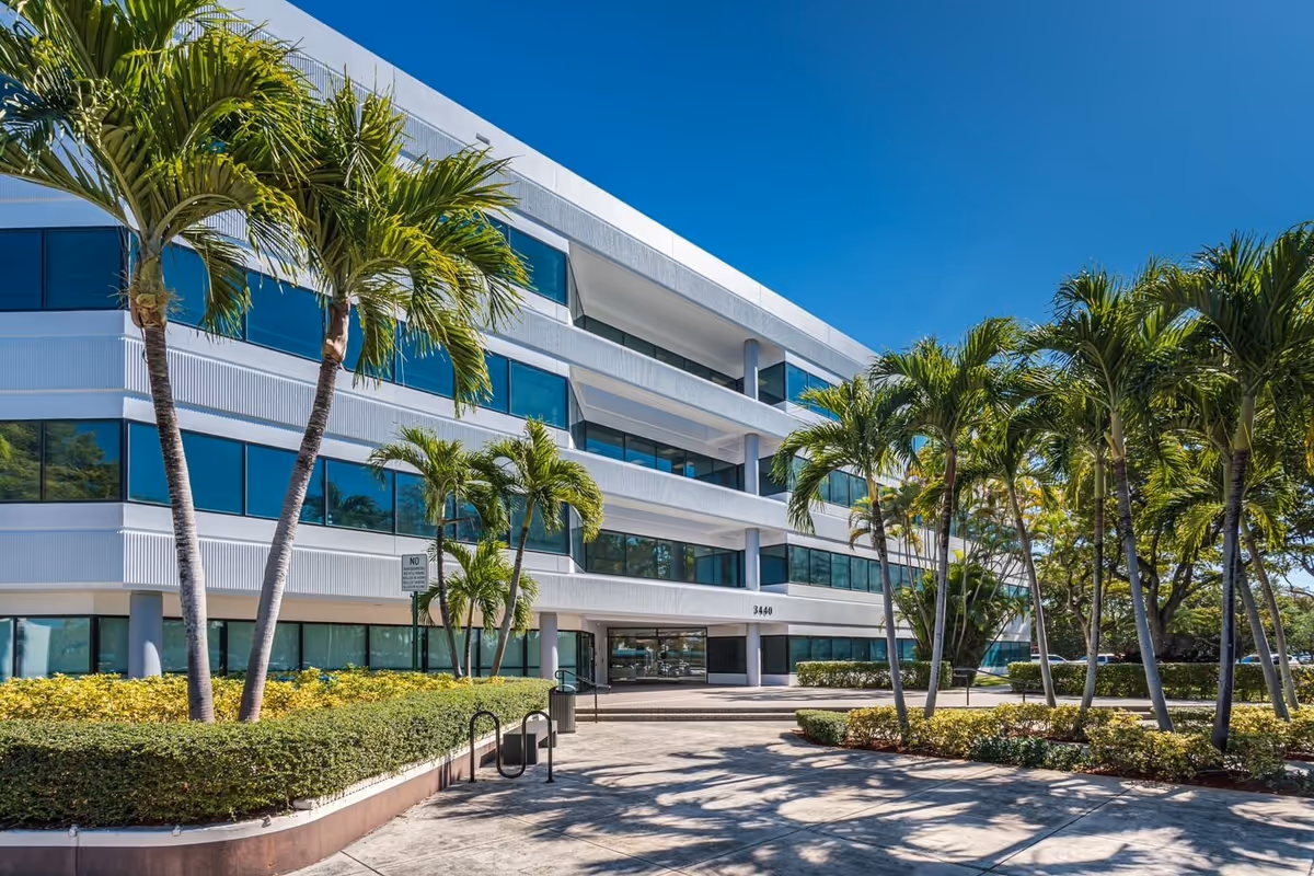 Modern white multi-story building with glass windows, surrounded by tall palm trees