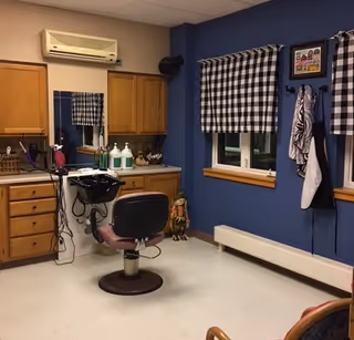 Salon area in a senior living facility with a barber chair, sinks, and blue walls.