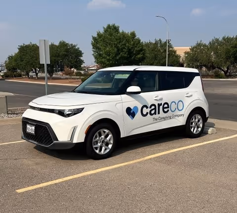 White CareCo-branded SUV parked in a parking lot with trees and buildings behind.