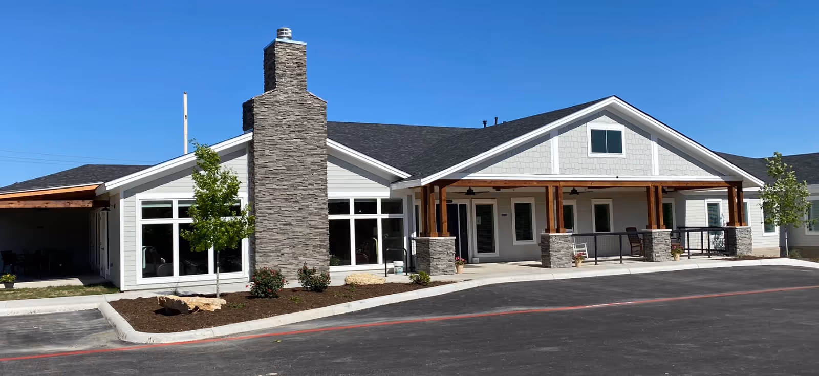 Single-story assisted living facility with stone chimney, white siding, and a covered front porch.