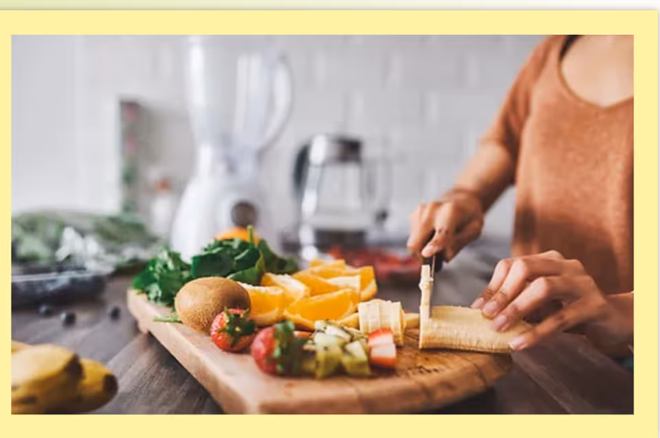 Person prepares assorted fruit on cutting board in a bright kitchen.