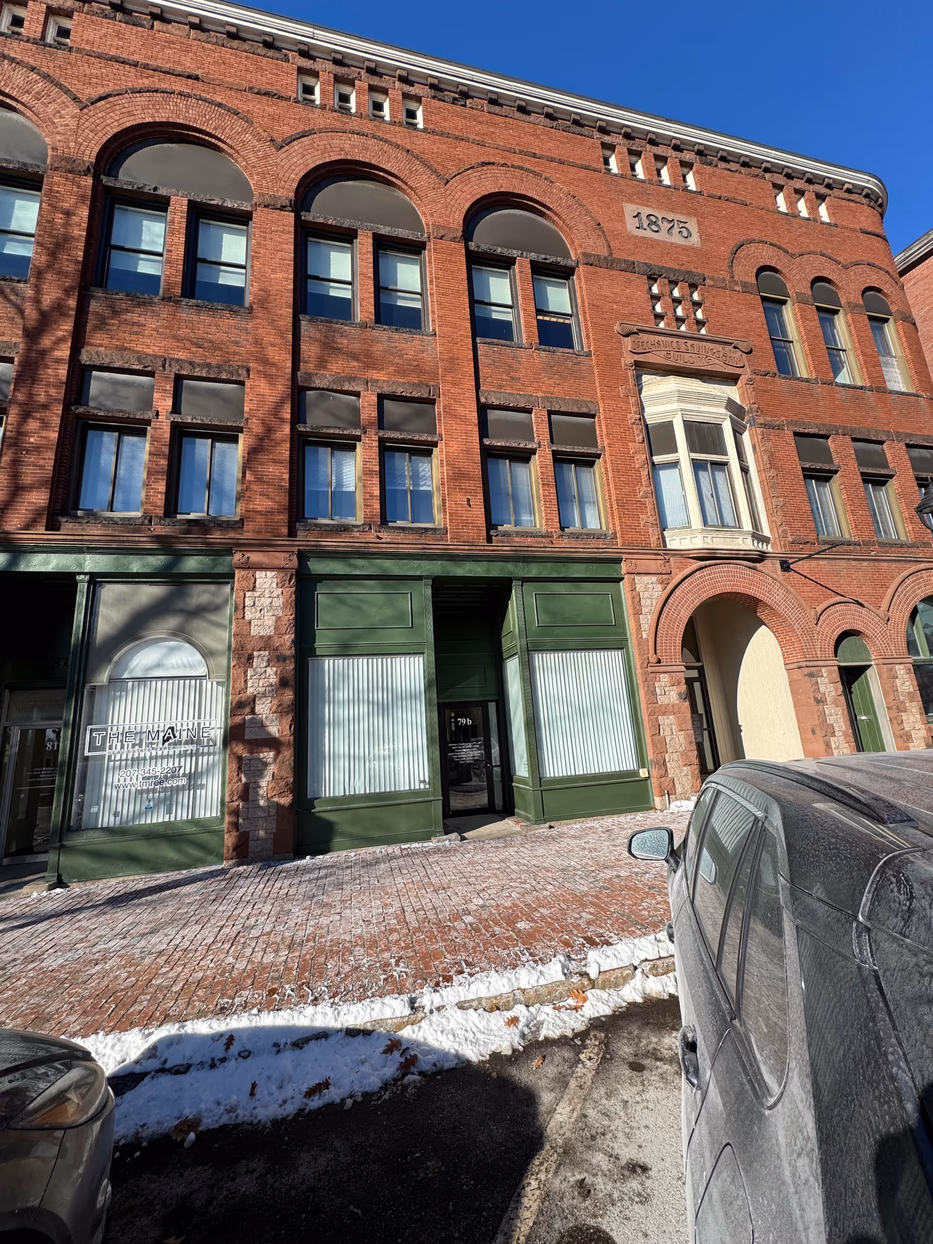 Brick building facade with arched windows and green storefronts along a snowy sidewalk.