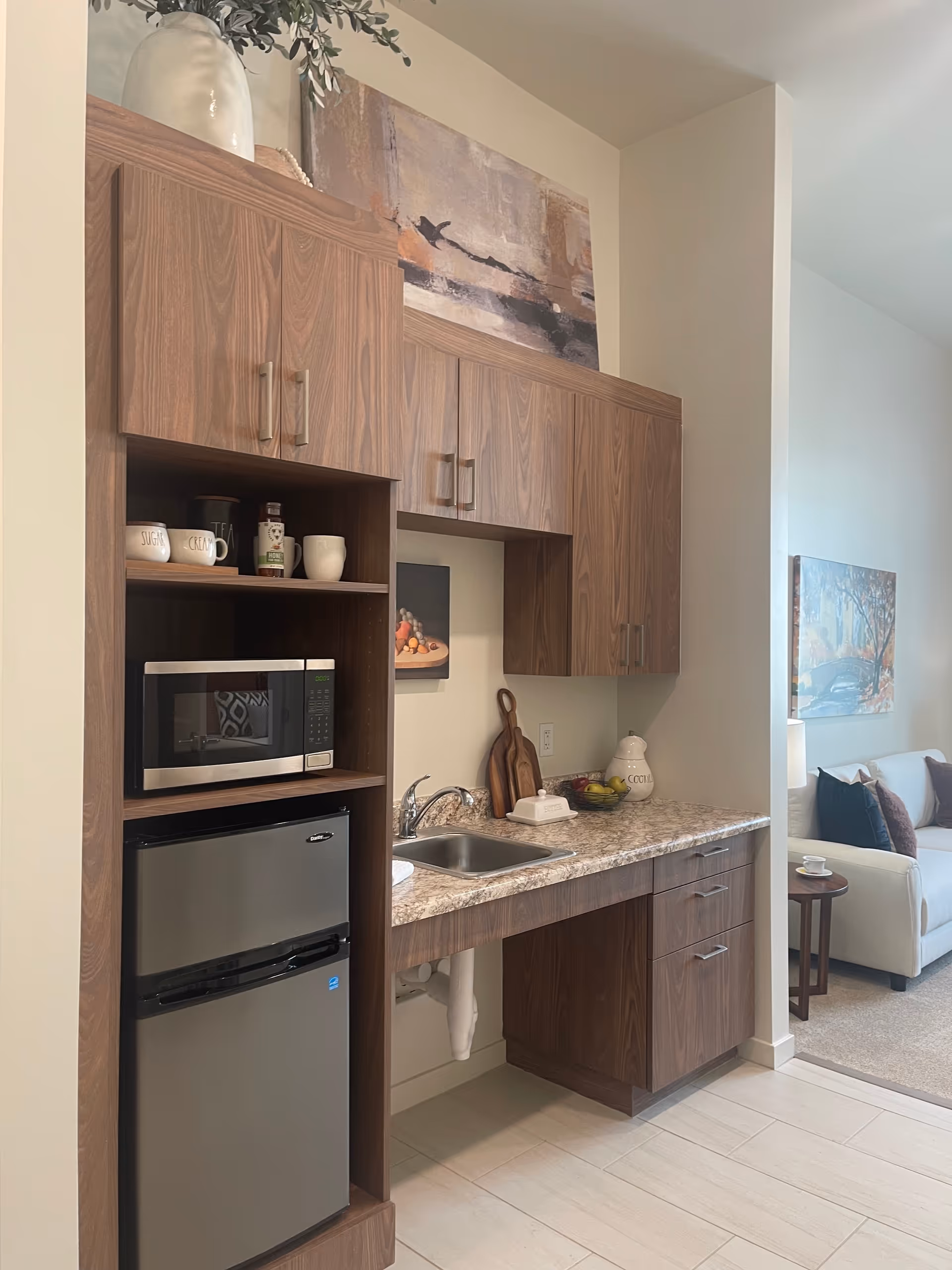 Wood-toned cabinets frame a compact kitchenette with microwave, sink, and mini-fridge.