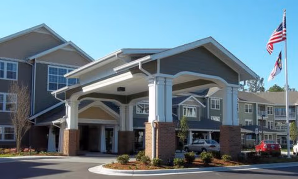 Front entrance of a multi-story senior living building with a covered porte-cochère and flagpoles.