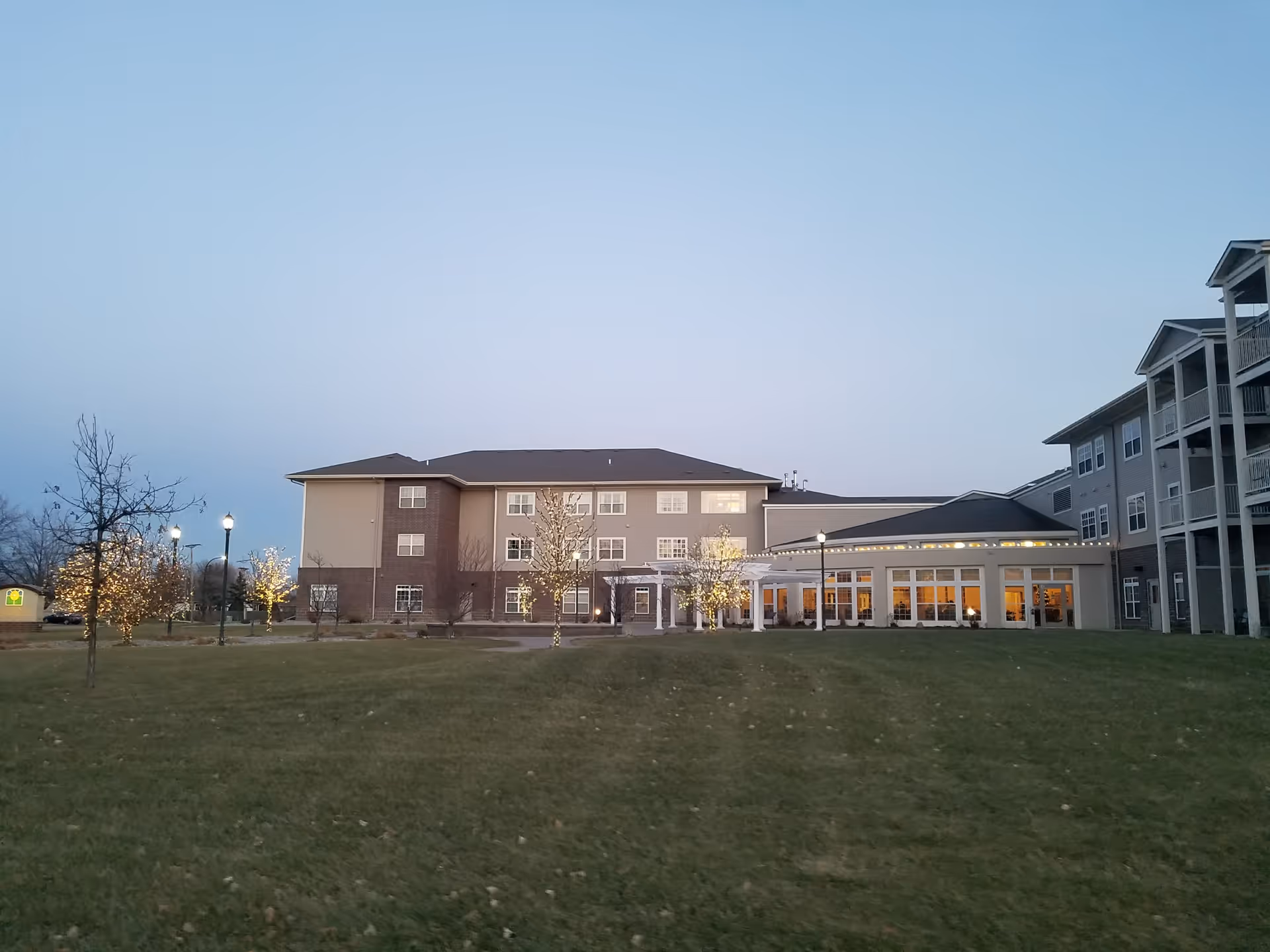 Exterior view of Eventide at Sheyenne Crossings with lawn, trees, and an illuminated entrance.