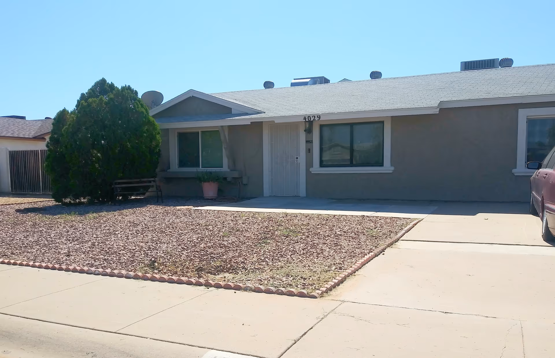 Single-story ranch-style home with a gravel front yard, driveway, covered porch and two front windows.