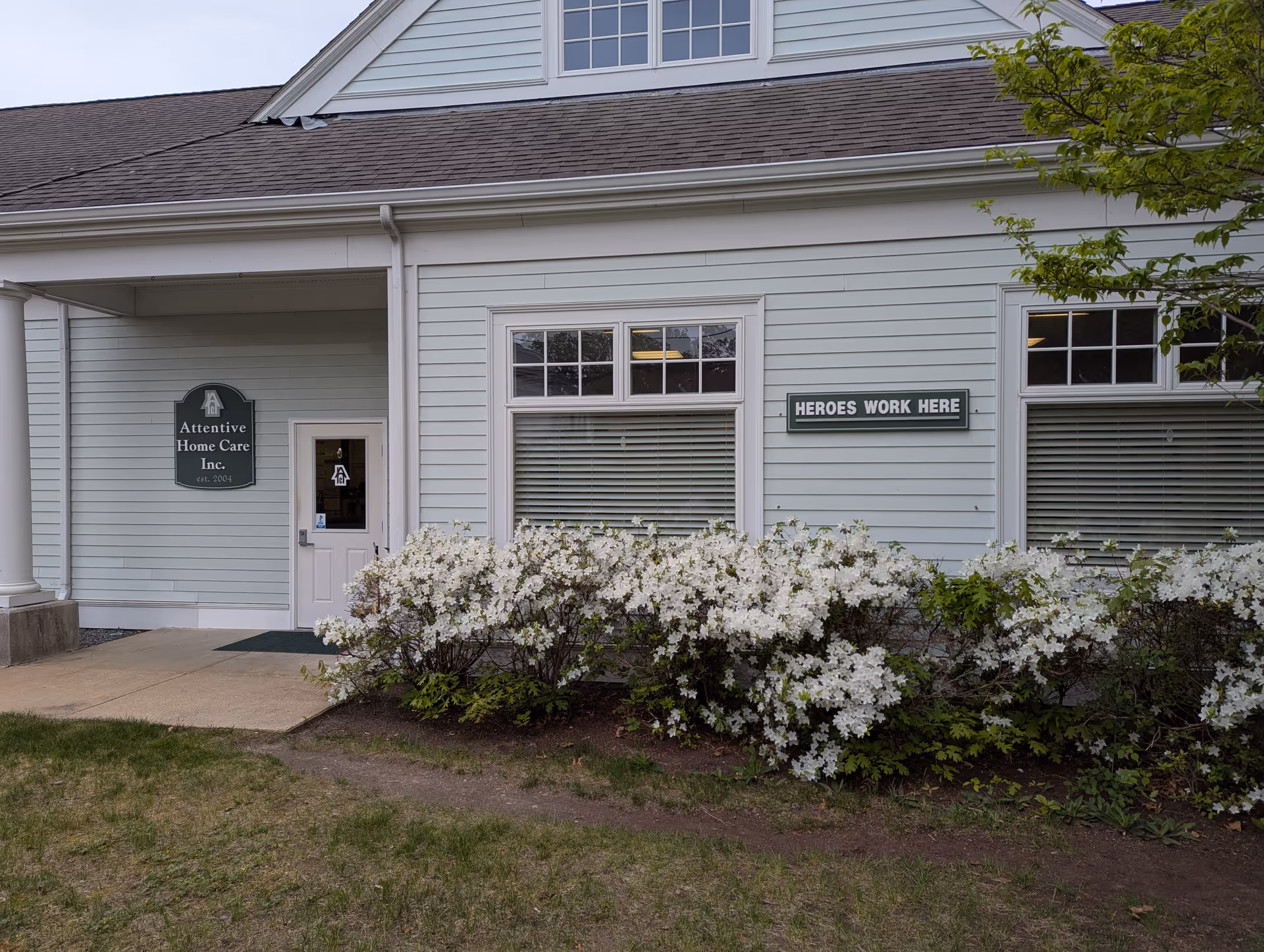 Light-blue building entrance with flowering shrubs and a 'Heroes Work Here' sign.