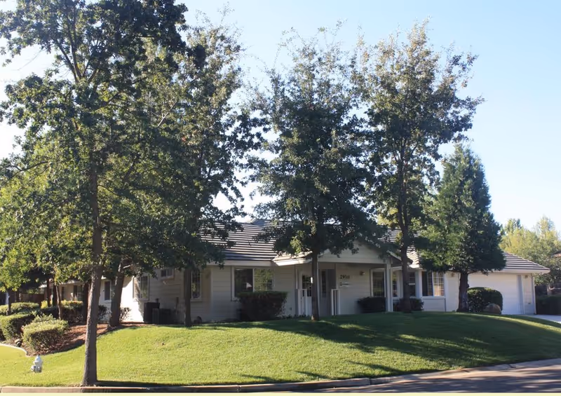A single-story senior living community building with a manicured lawn and trees.