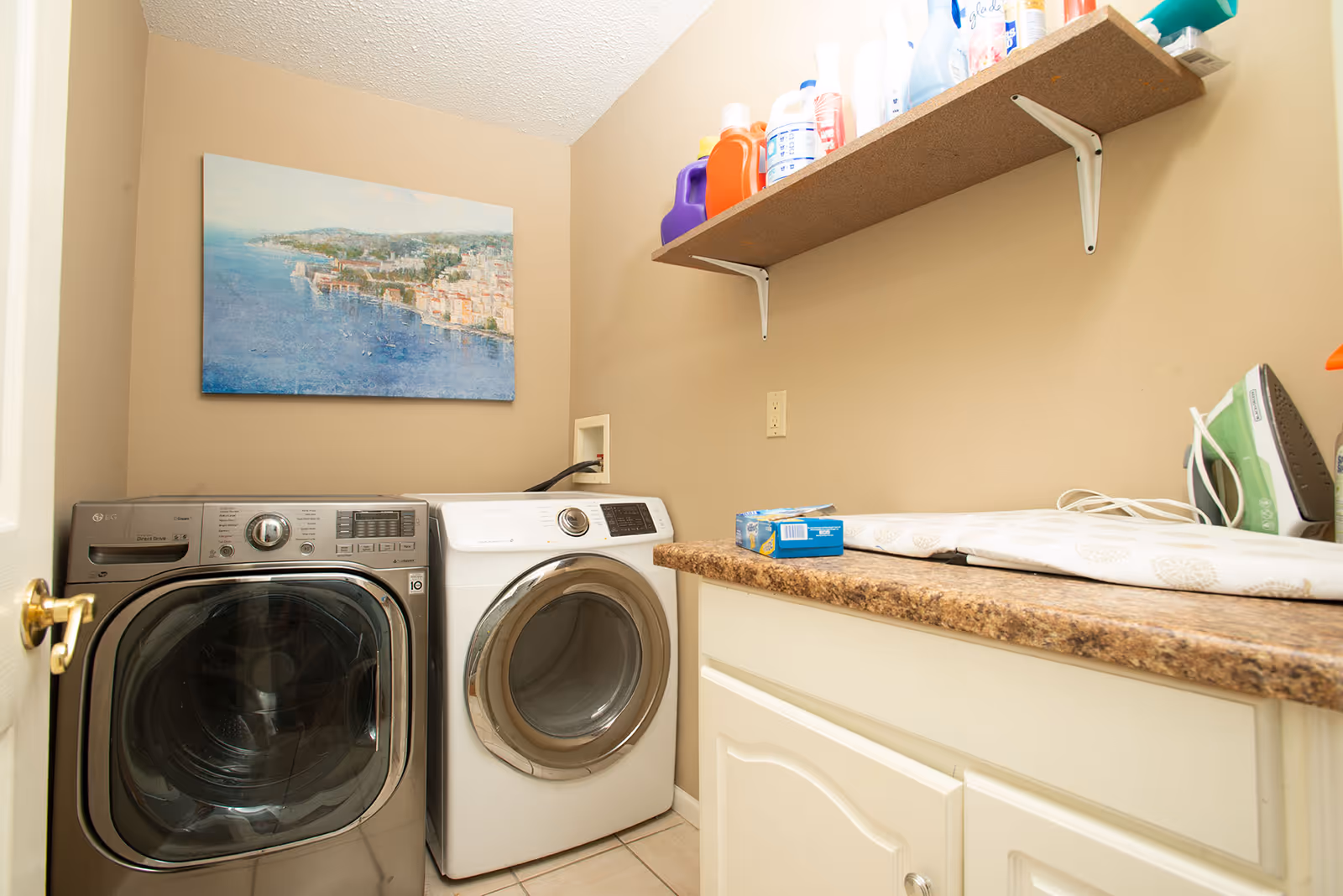 Laundry room with front-loading washer, dryer, counter, and cleaning supplies.
