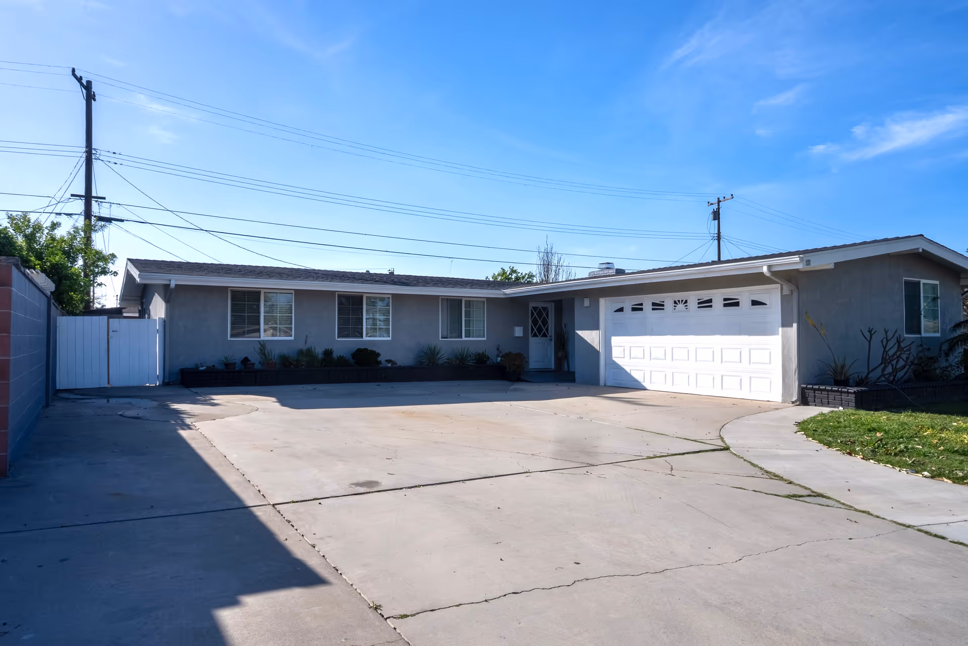 Single-story gray house with attached garage, long driveway, and minimal landscaping.