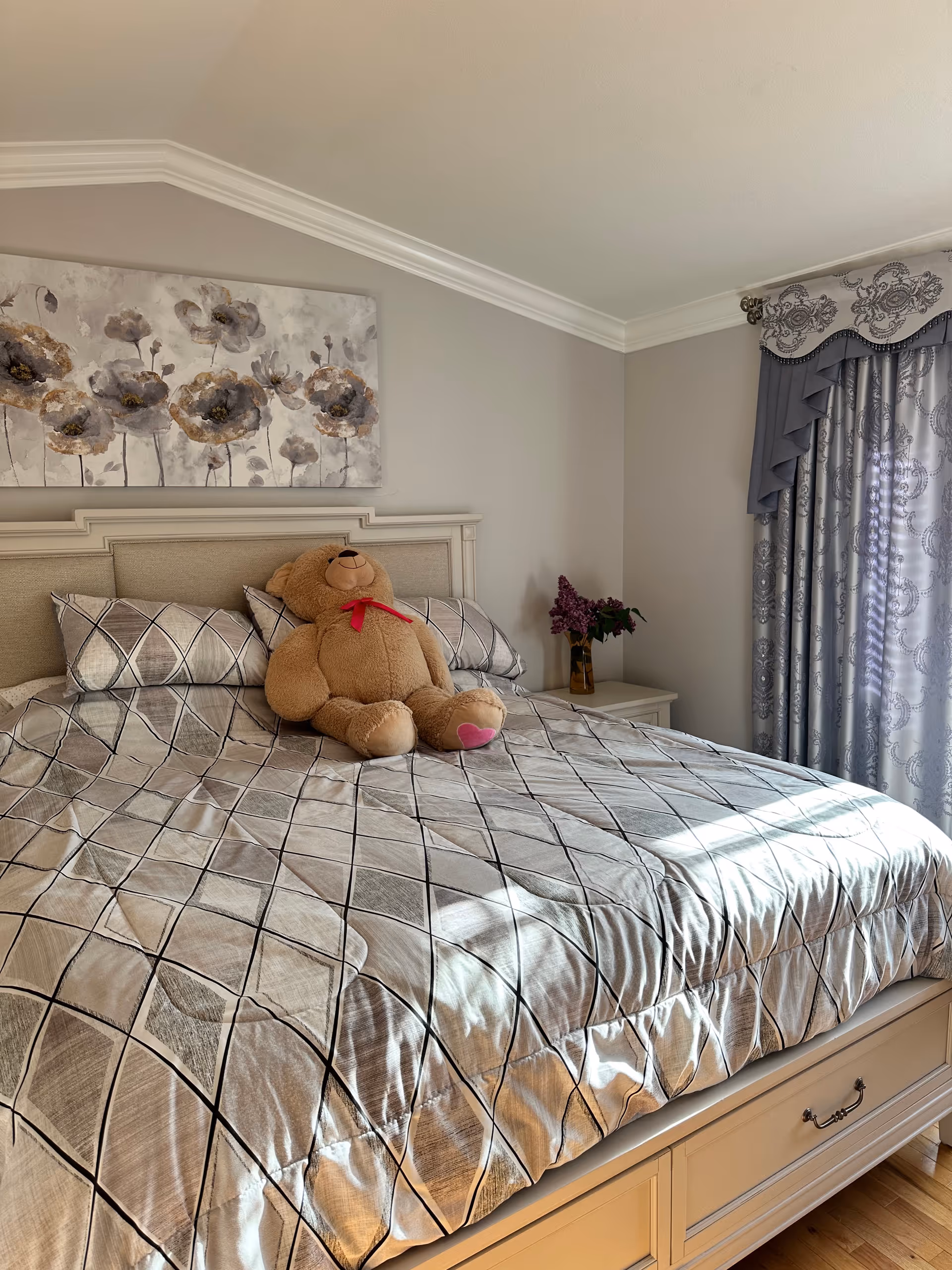 Cozy bedroom with a large bed, teddy bear, and decorative curtains.