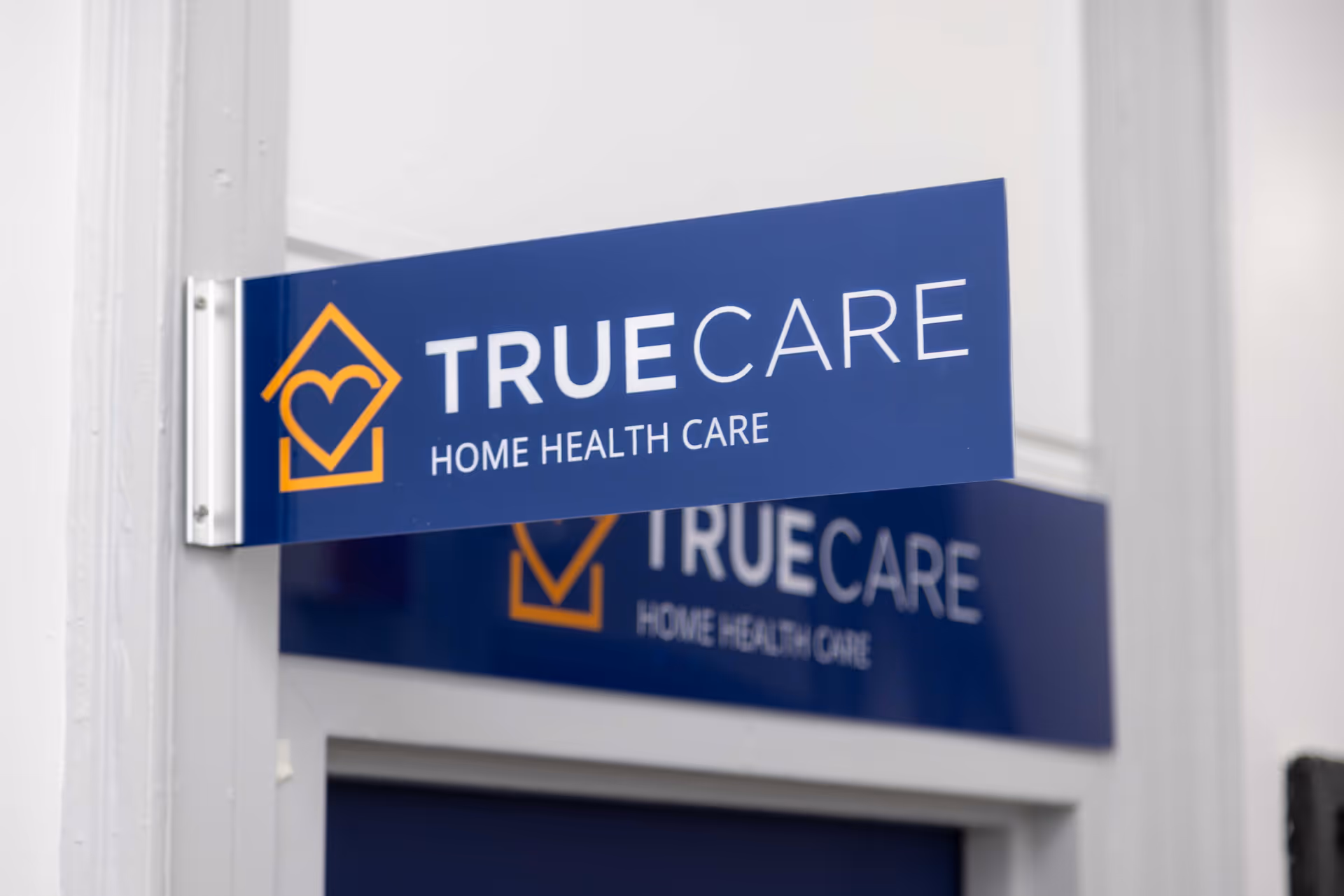 Blue TRUECARE sign with orange logo reading TRUECARE HOME HEALTH CARE on building exterior