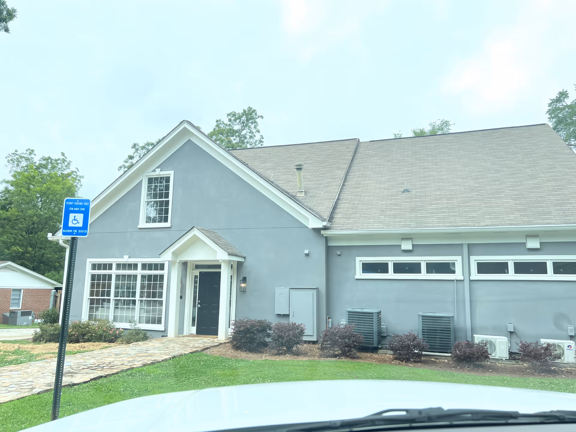 Front view of a gray senior living facility with handicap sign and HVAC units.