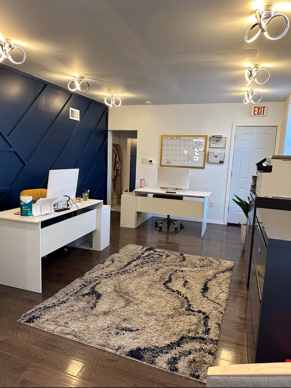 Interior reception area with white desks, blue accent wall panels, and a patterned rug.
