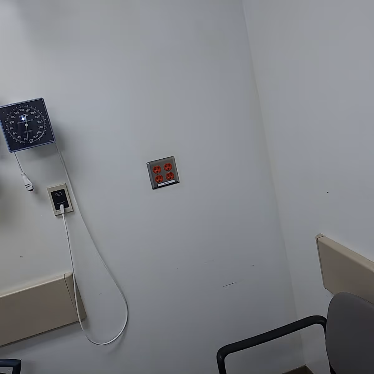 A hospital exam corner with a wall-mounted blood pressure gauge and outlet.