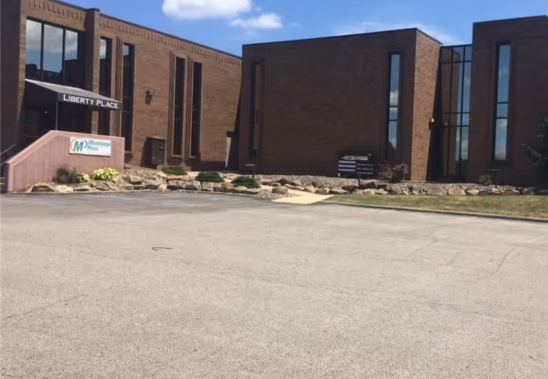 Exterior brick building with tall windows, ramp entrance, and landscaped rocks.