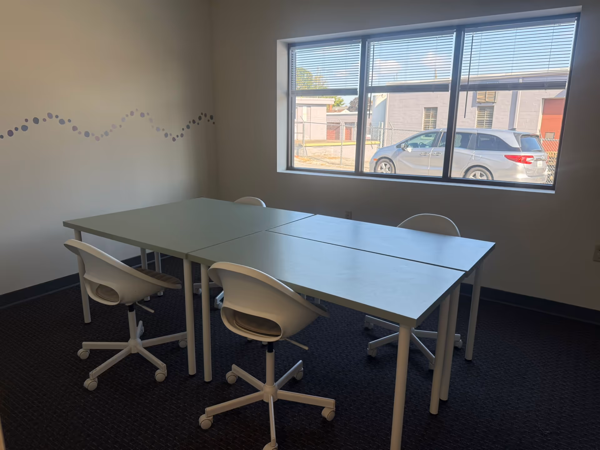 A clean interior room with white tables and chairs by a large window.