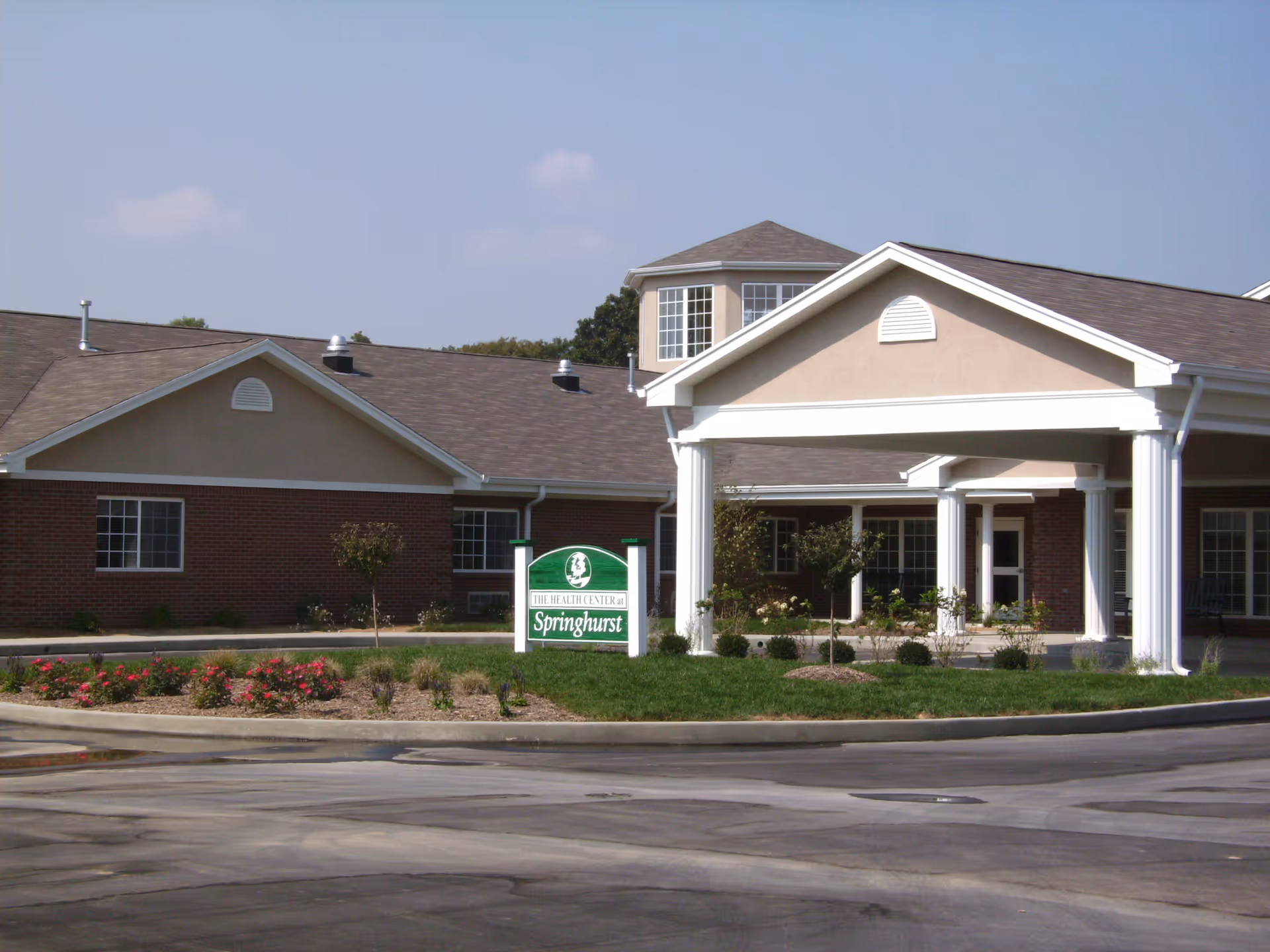 Exterior view of Springhurst senior living campus with brick building, white columns, and a green sign.