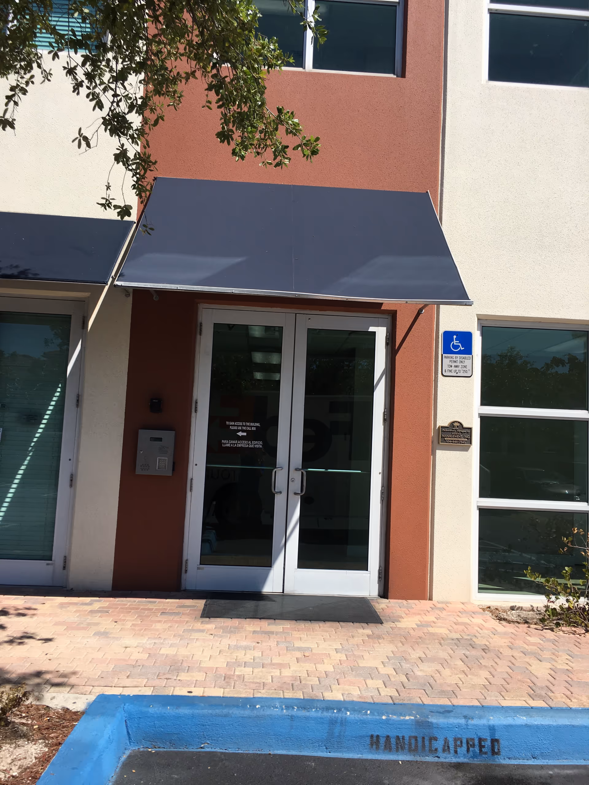 Front entrance of a senior living facility with glass doors, an awning, and a wheelchair sign.