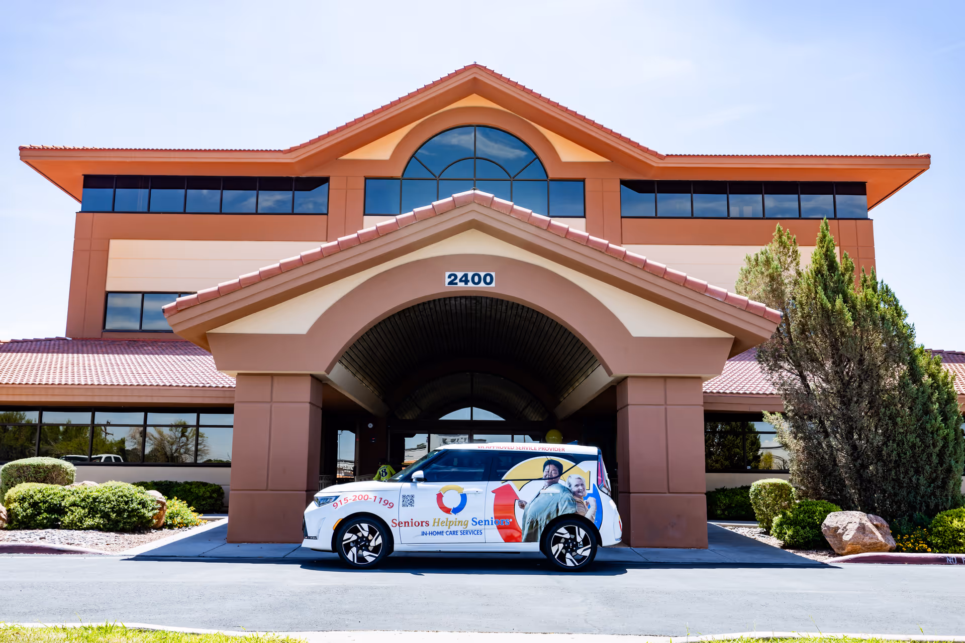 Sunlit senior living building with a covered entrance and a van branded 'Seniors Helping Seniors'.