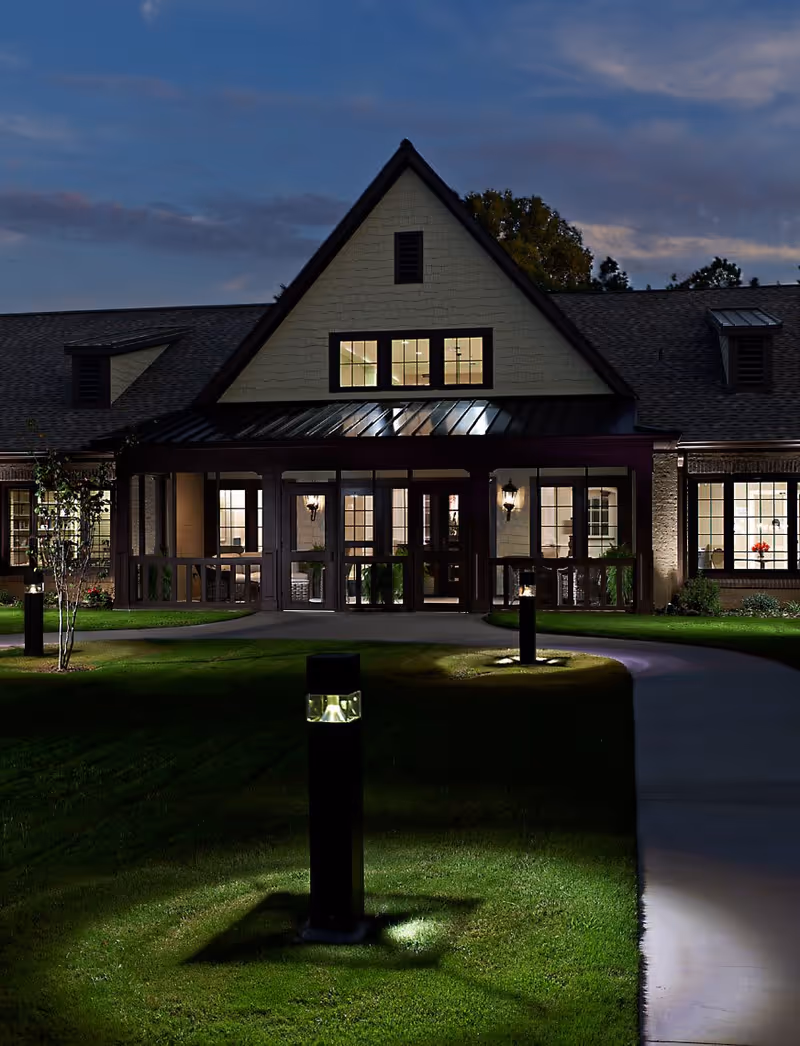Illuminated front entrance and facade of a residential building at dusk with a lit walkway and bollard lights.