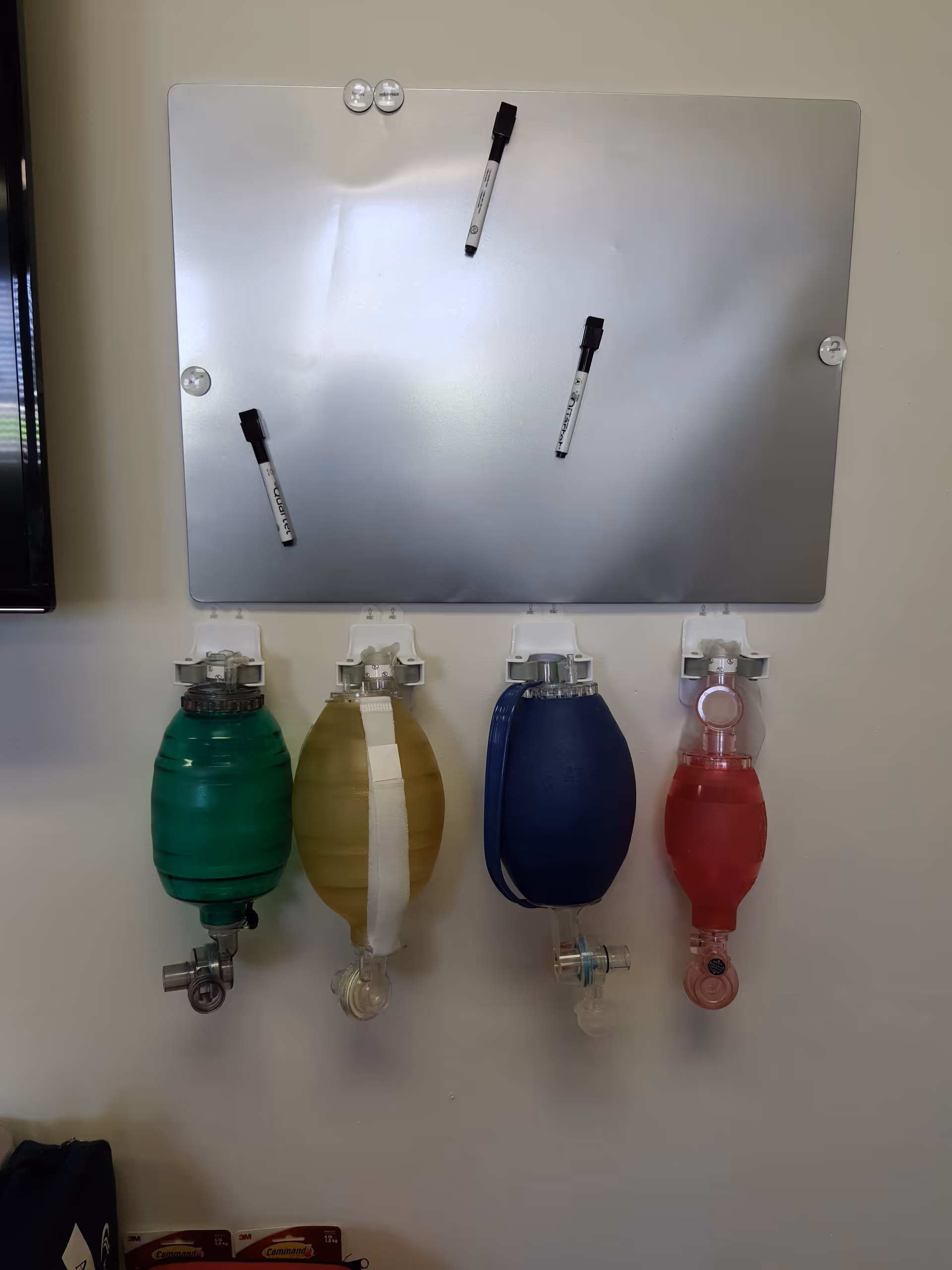 Four color-coded oxygen tanks mounted on a wall beneath a metal panel.