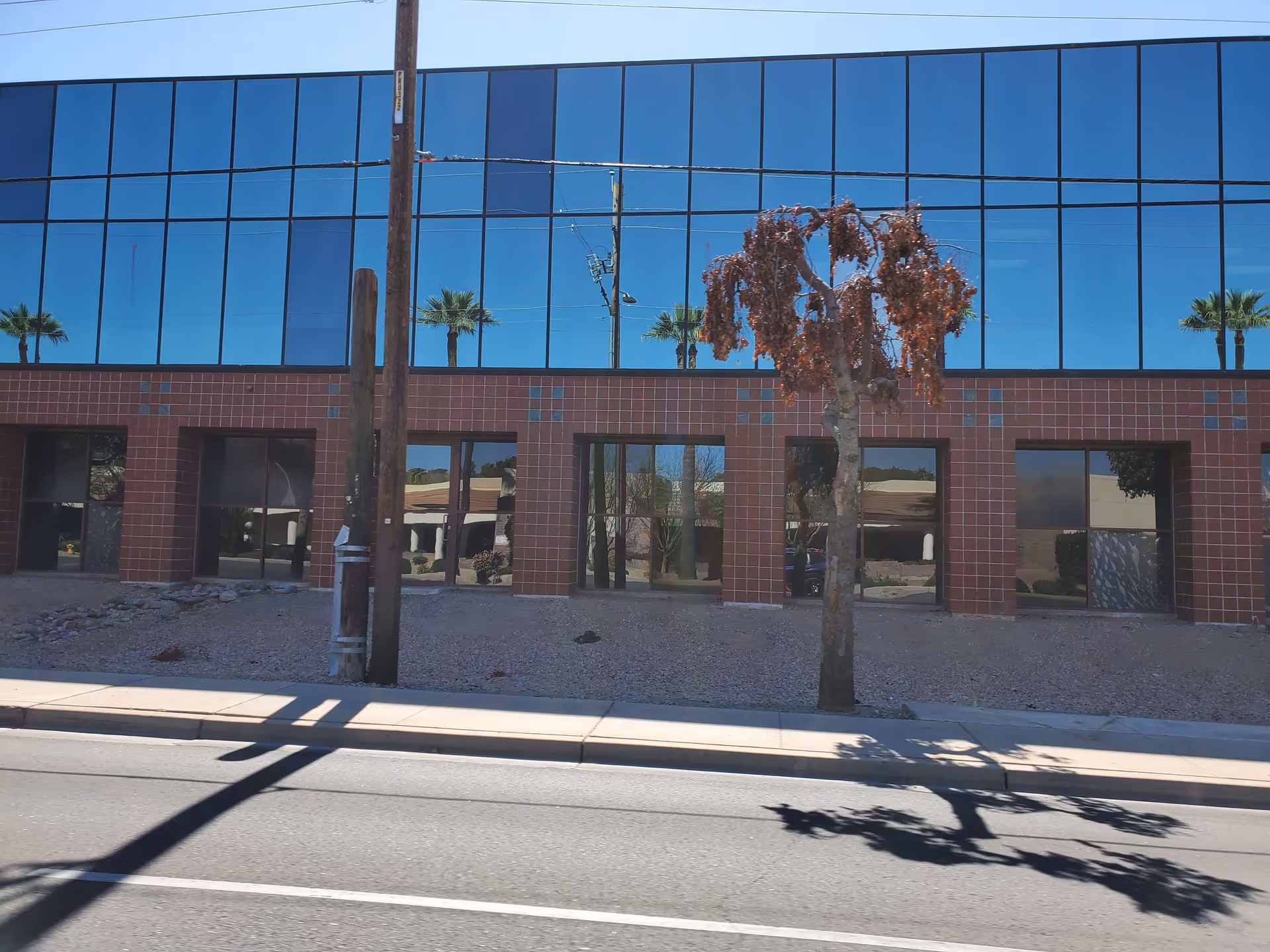 Modern glass-fronted building with brick accents and a sidewalk in front.