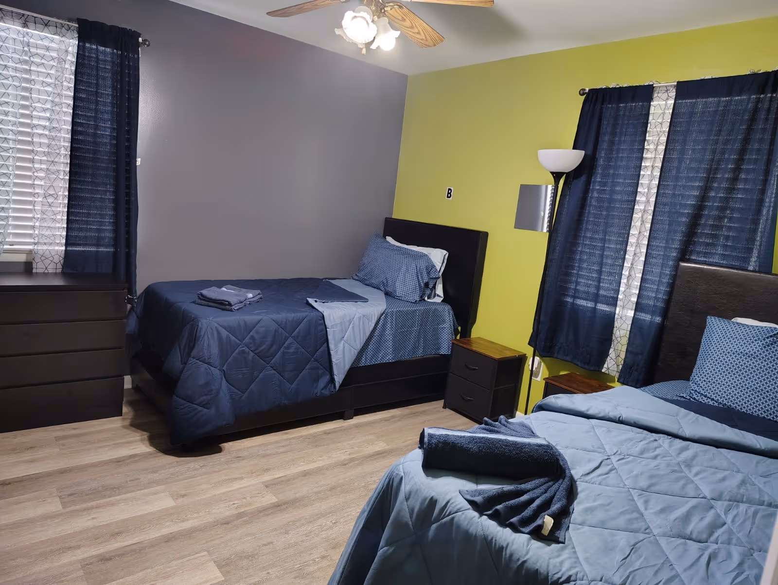 Two twin beds with blue bedding and nightstands in a lime-green and gray bedroom.