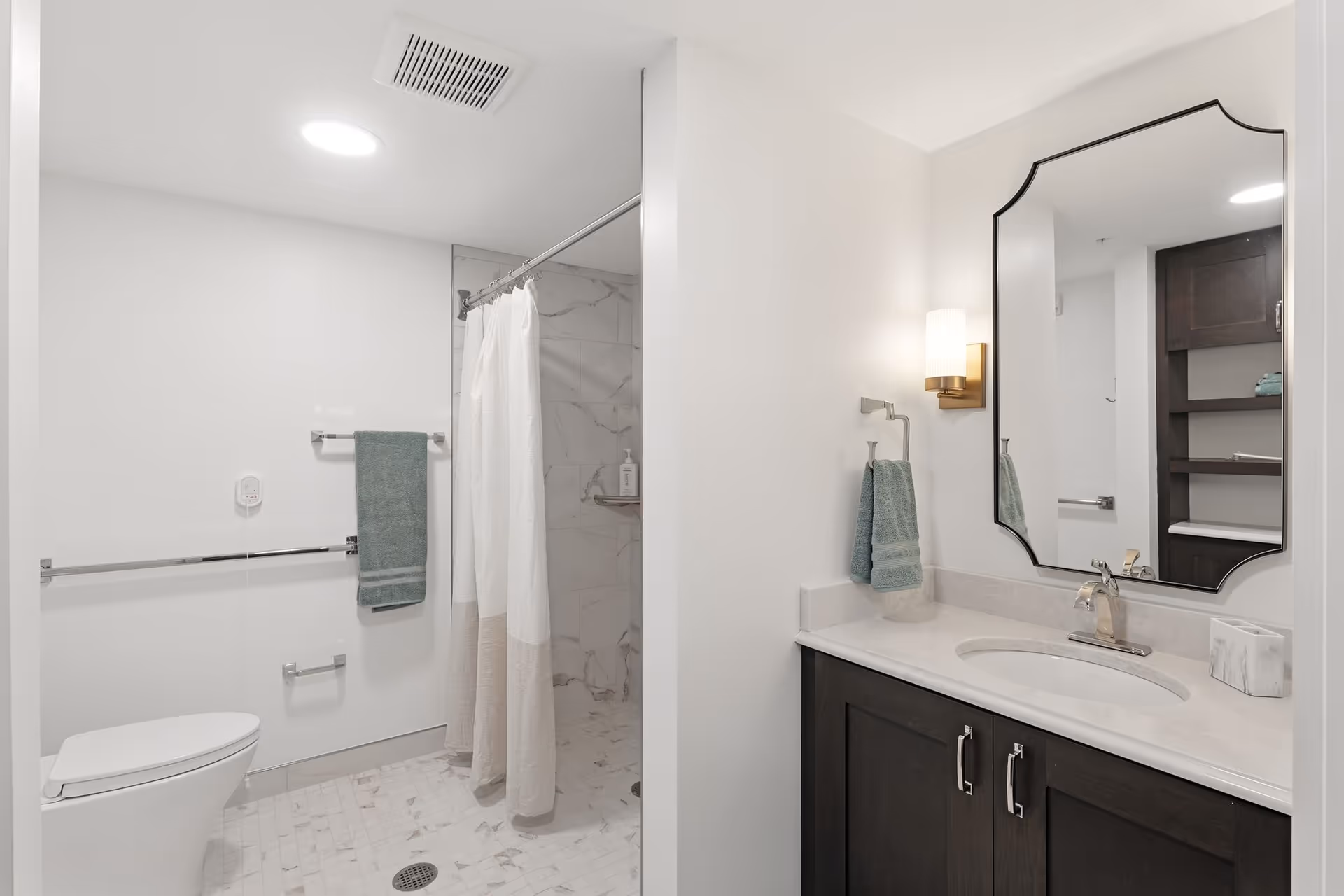 Bright bathroom with shower, toilet, and vanity in a senior living facility.