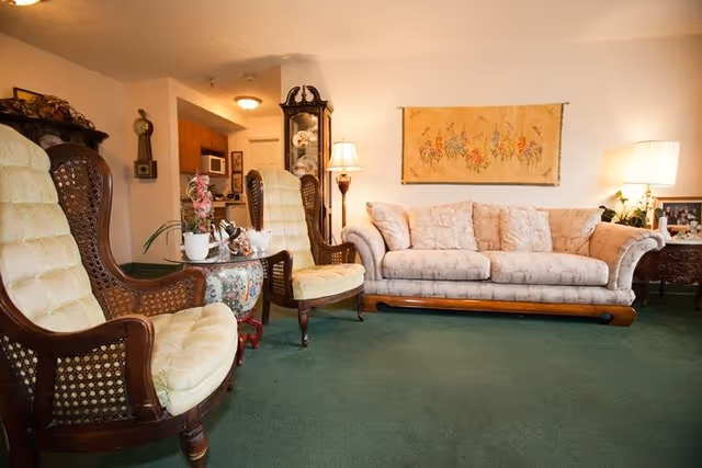 Cozy senior facility living room with sofa, chairs, lamps, and wall art.