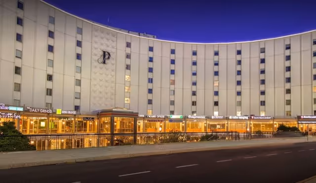 Curved white building exterior with illuminated storefronts along the ground floor at dusk.