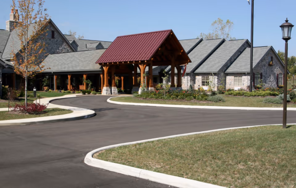 Exterior view of The Inn at Olentangy Trail showing a large stone building with a covered entrance supported by wooden beams, surrounded by landscaped greenery and a curved driveway.