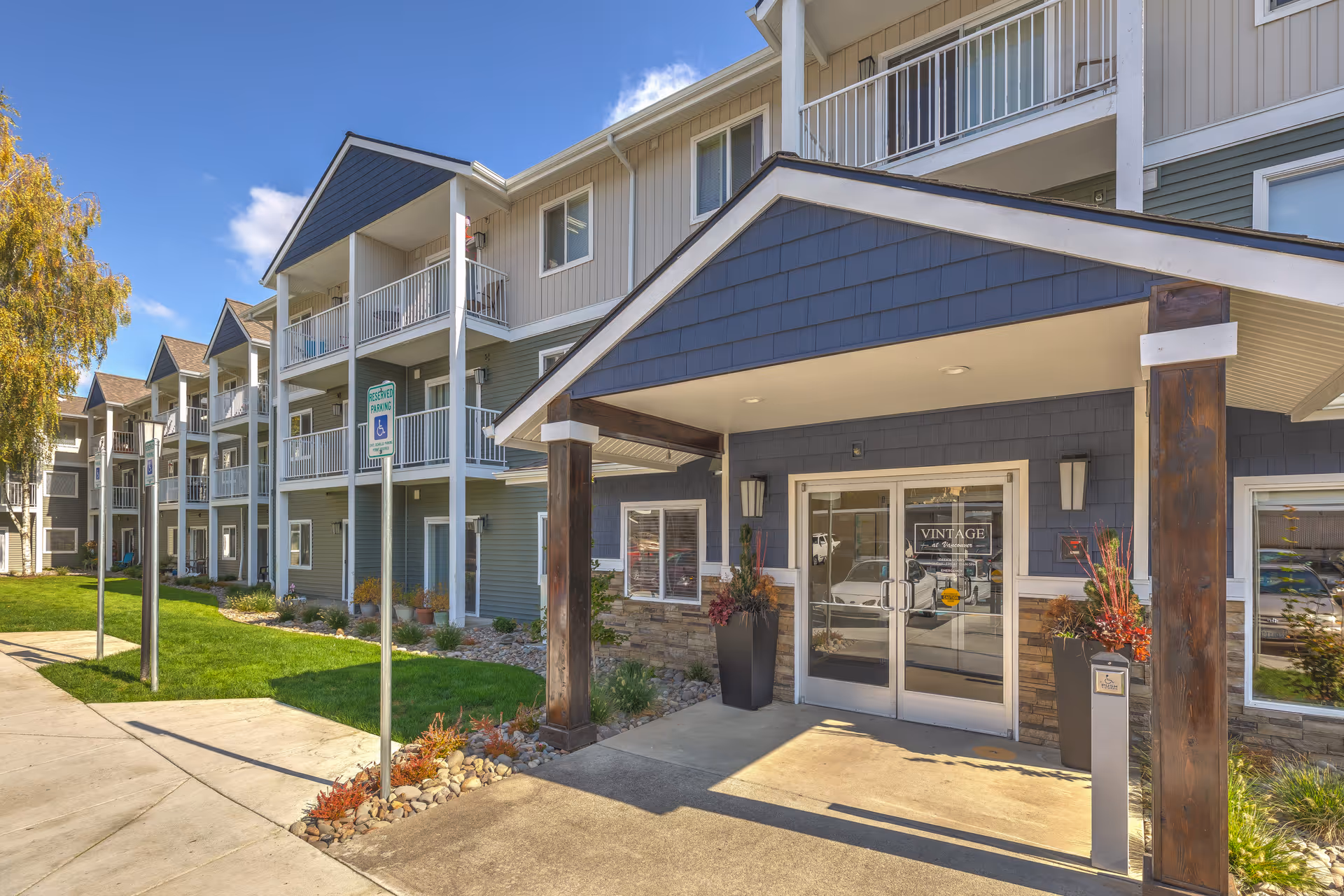 Multi-story senior living building exterior with covered entrance and balconies along a landscaped walkway.