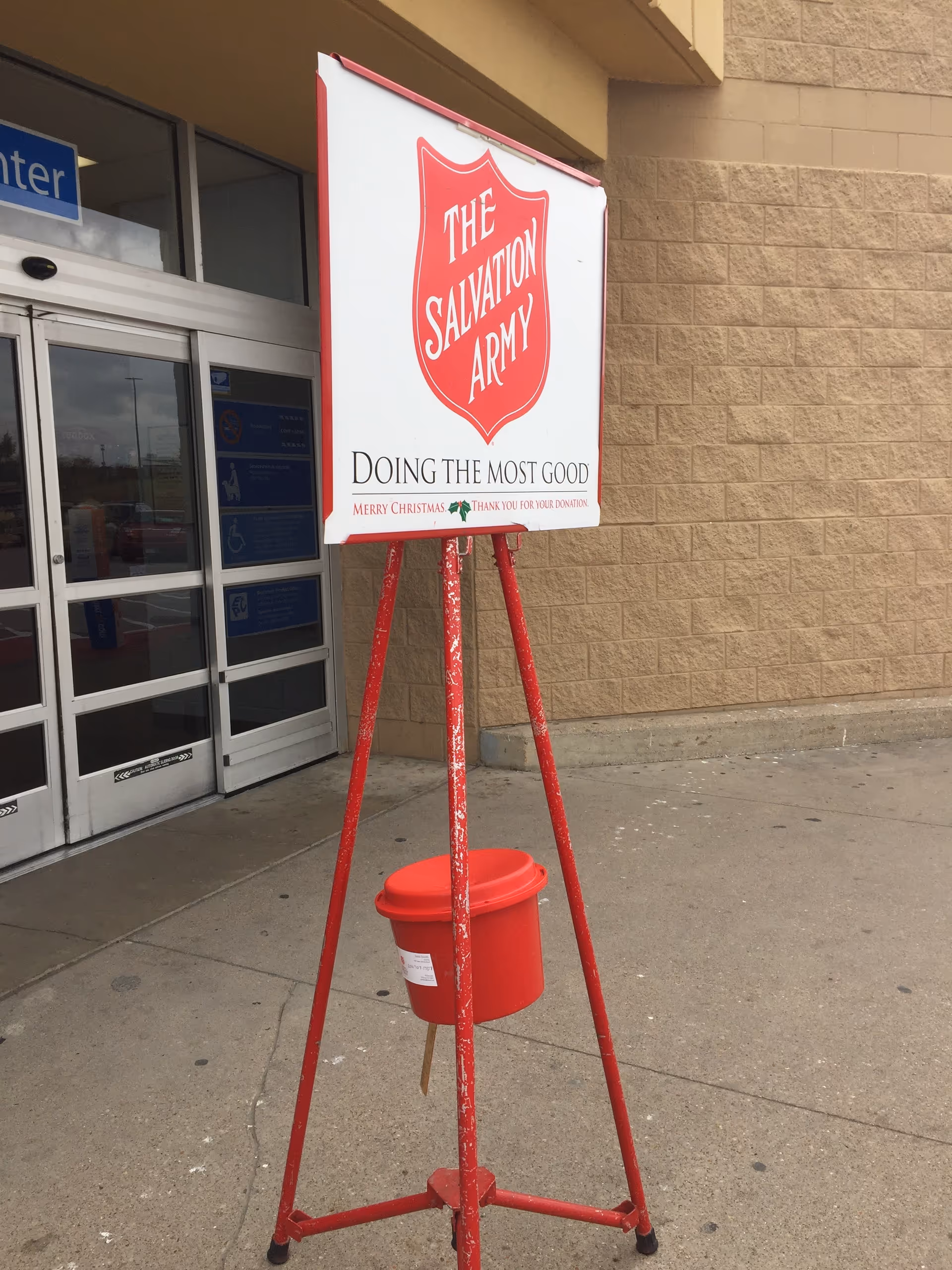 Salvation Army donation sign on a red tripod outside a storefront.