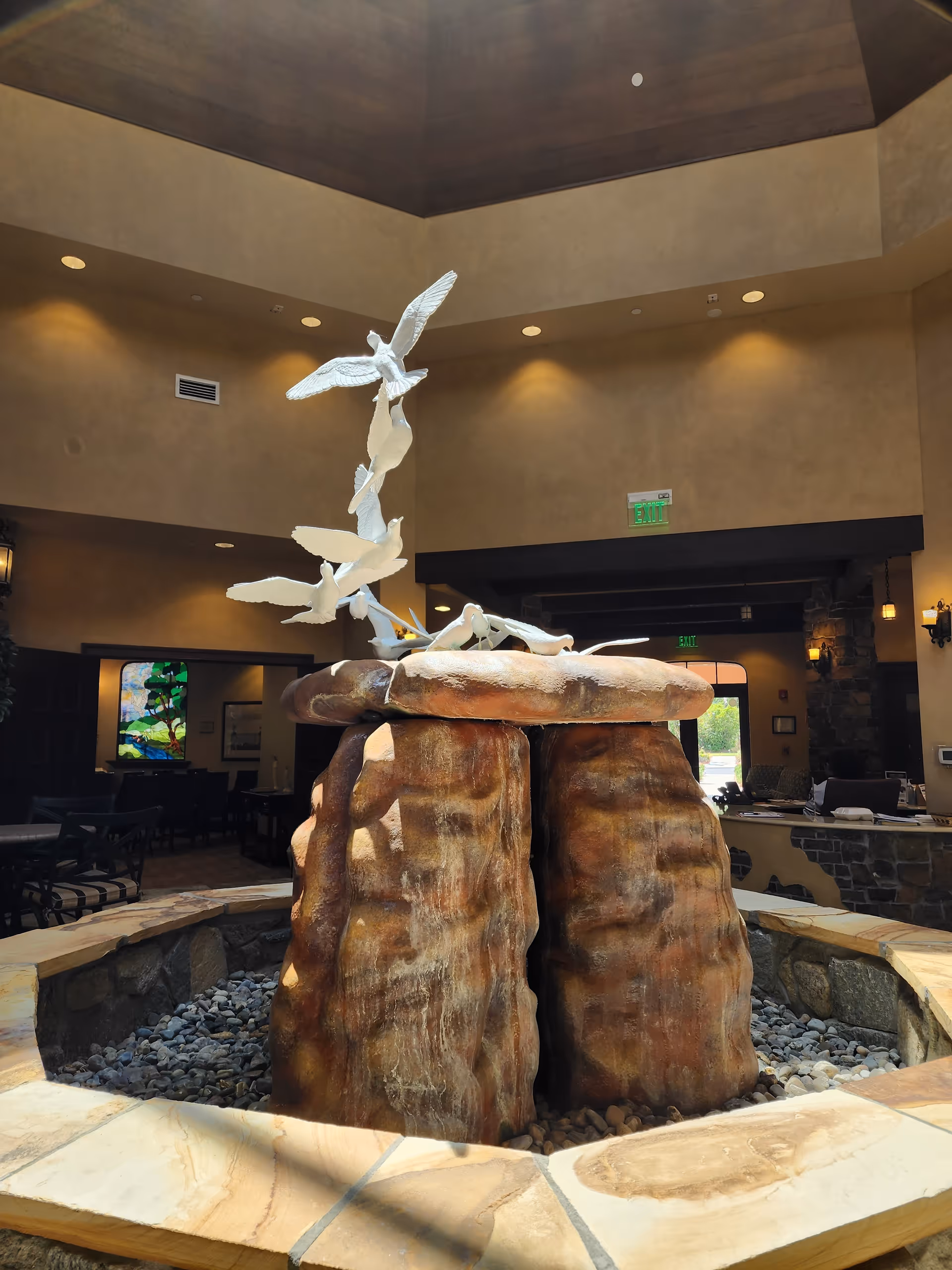Indoor lobby with a large stone fountain centerpiece and white bird sculpture.