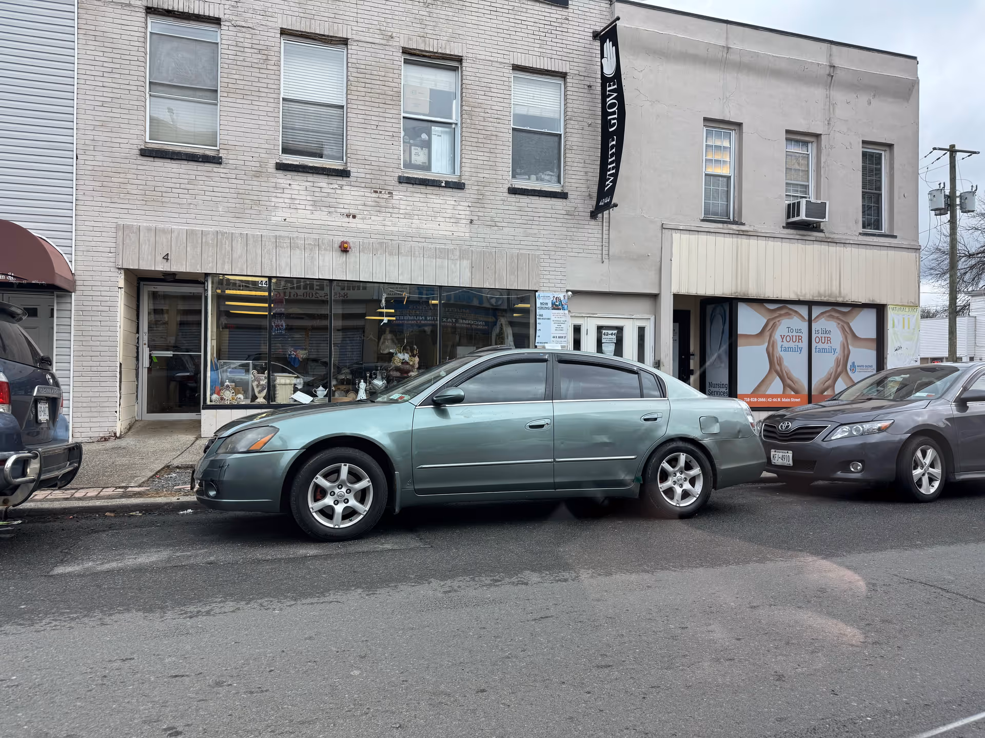 Street view of storefronts with a vertical 'White Glove' banner and parked cars.