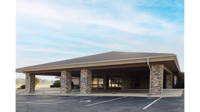Covered brick entrance to a senior care facility with a parking lot.