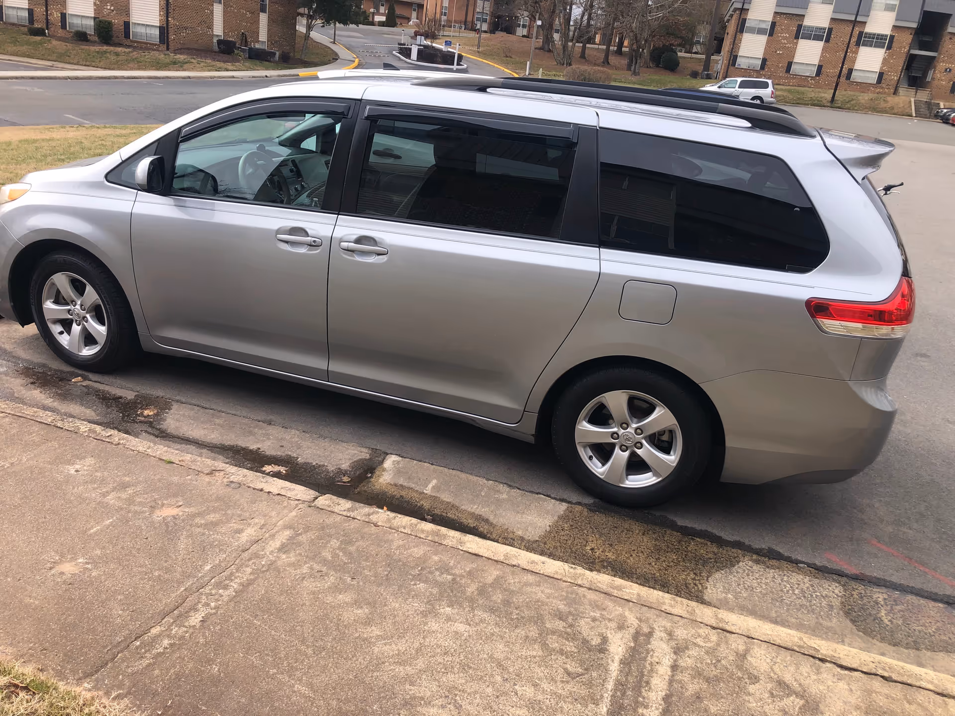 Silver minivan parked along curb with apartment buildings in the background