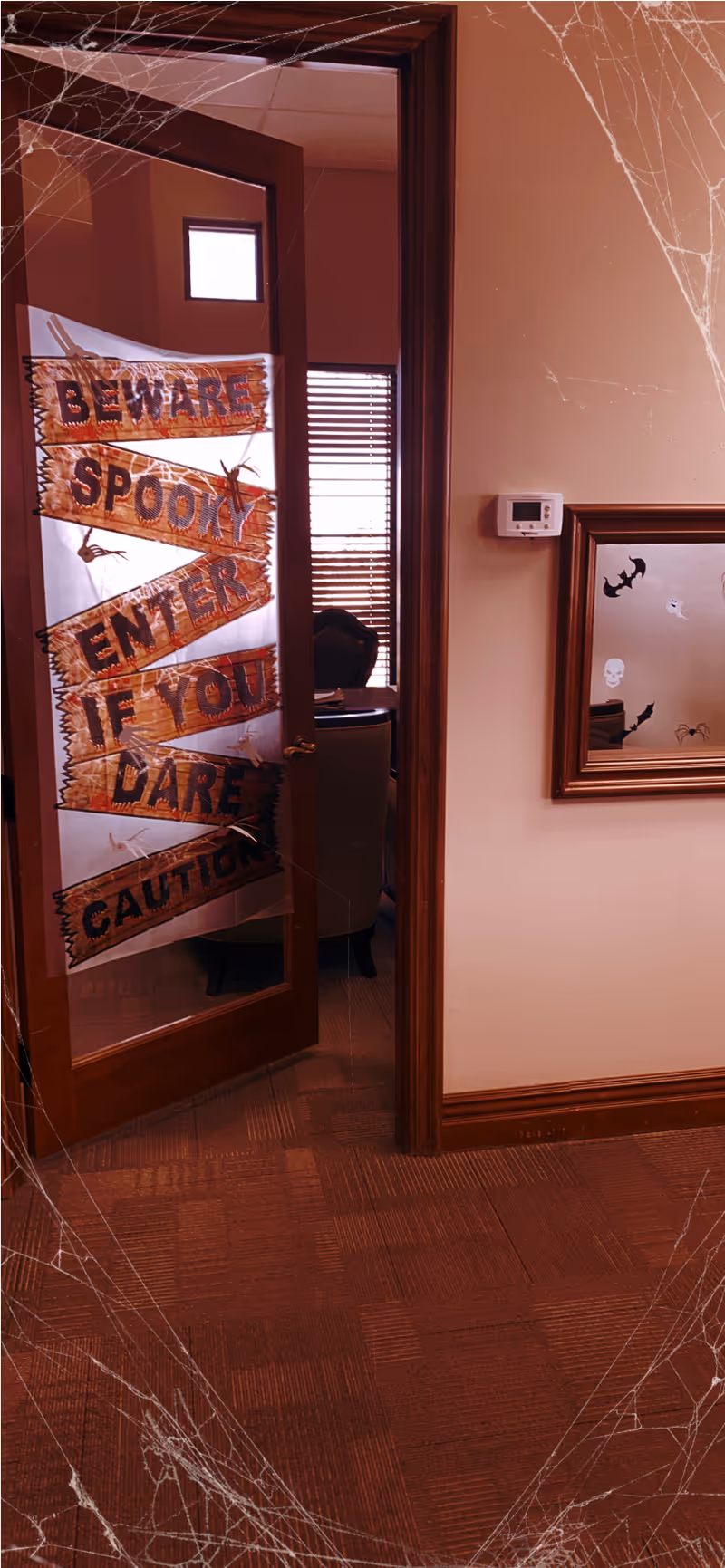 Doorway decorated with BEWARE SPOOKY ENTER IF YOU DARE sign in a hallway.