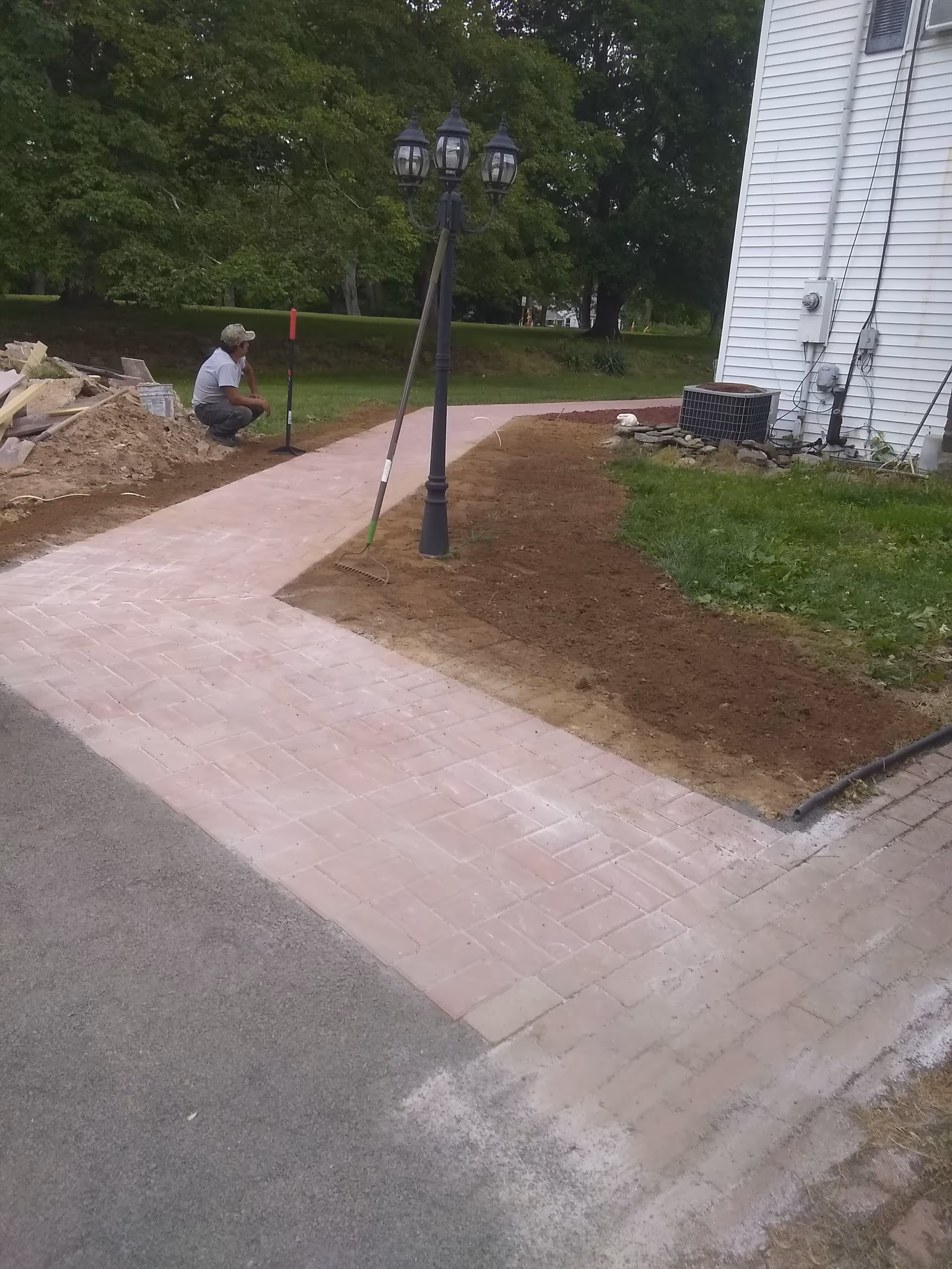 A worker crouches beside a pink brick walkway under construction outside a white building.
