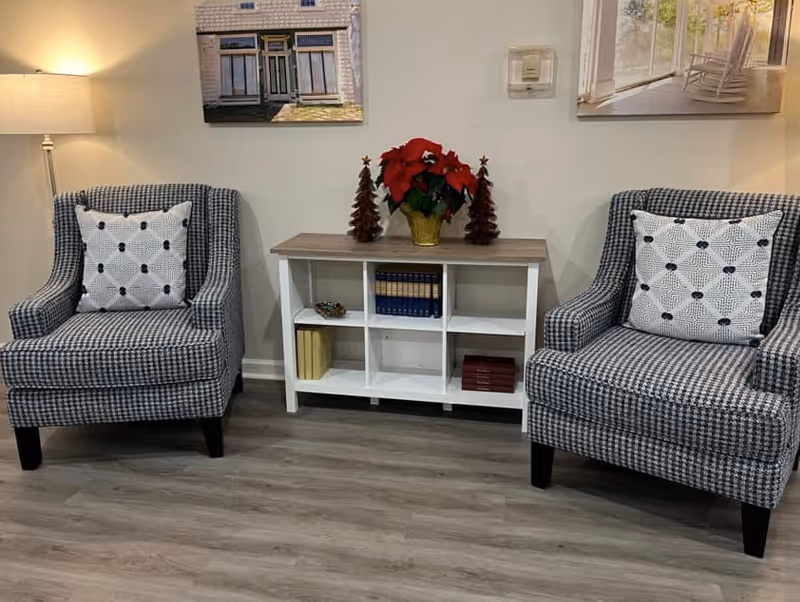 Two plaid armchairs flank a white cubby shelf with a poinsettia indoors.