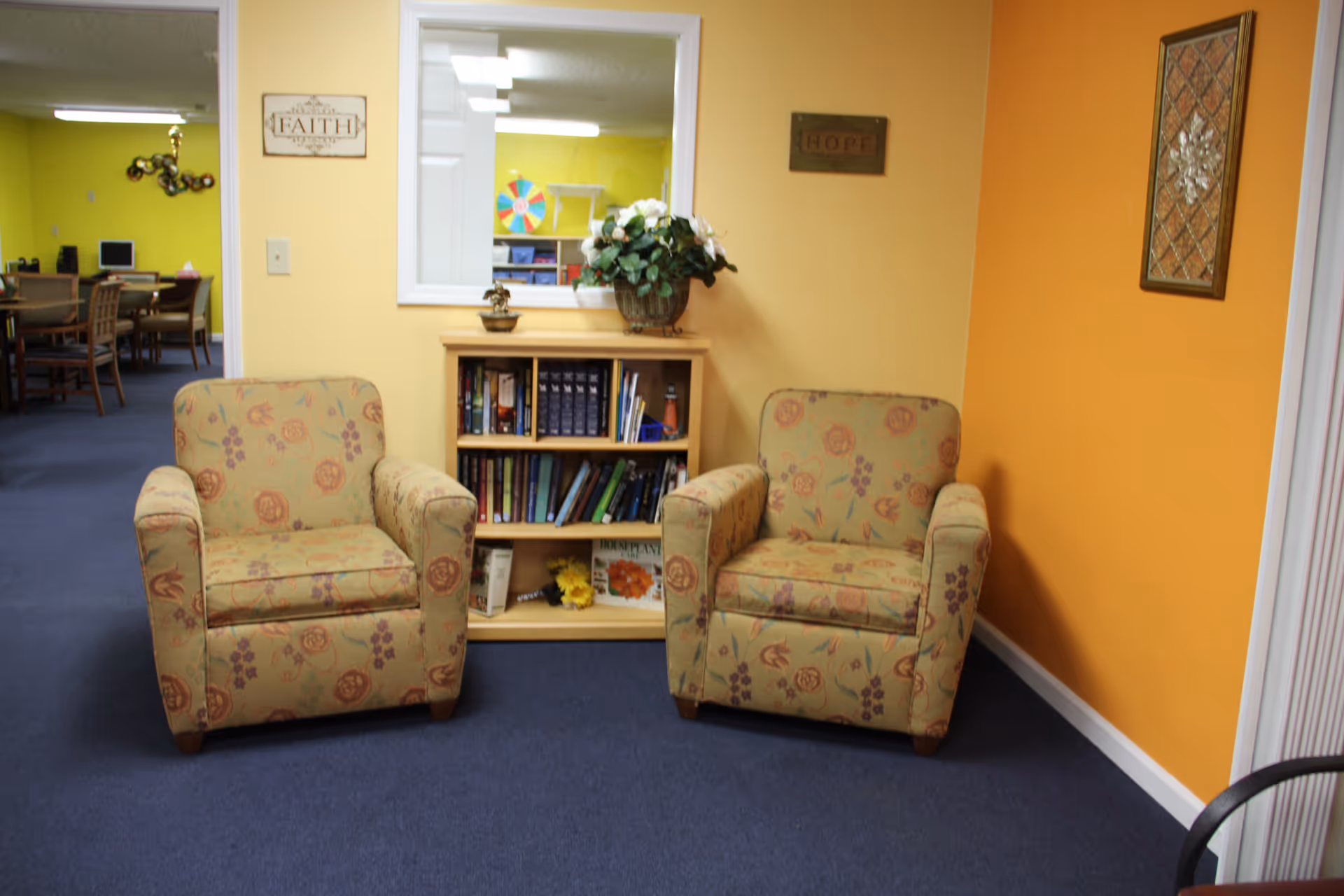 Two floral armchairs flank a small bookshelf in a bright interior lounge.