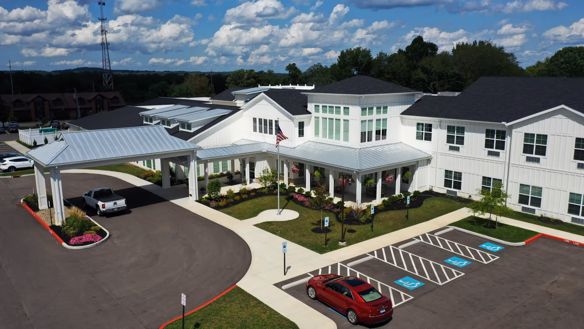 A modern white senior living facility with a covered entrance, parking, and landscaped grounds.