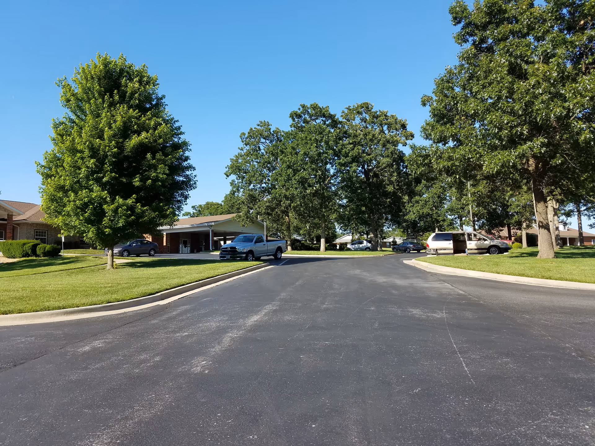Curving driveway leads to Lacoba Homes entrance with trees and parked cars.