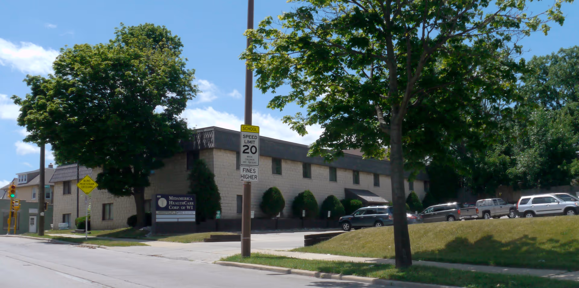 Exterior view of Mid America Healthcare facility with trees, cars, and a sign along the street.