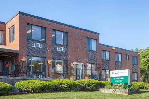Exterior view of a brick senior living center with a sign and trimmed hedges.