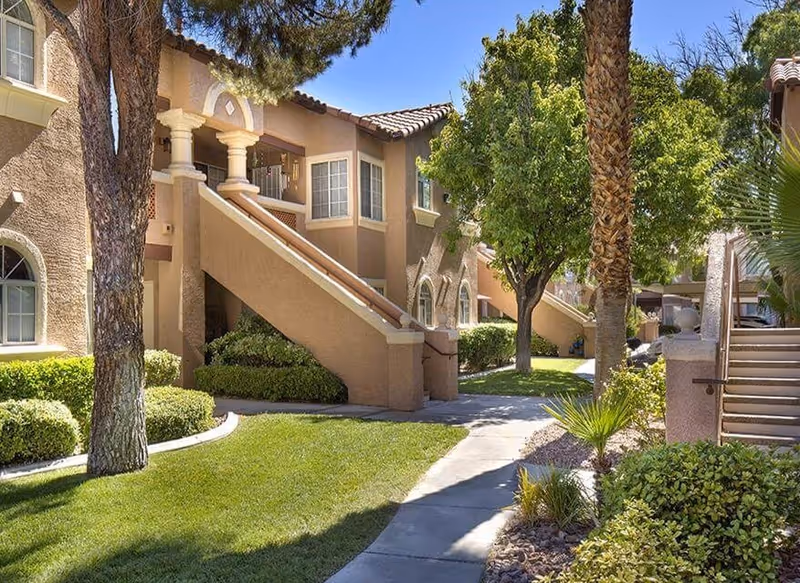 Exterior view of a tan senior living building with staircases, arches, and landscaping.