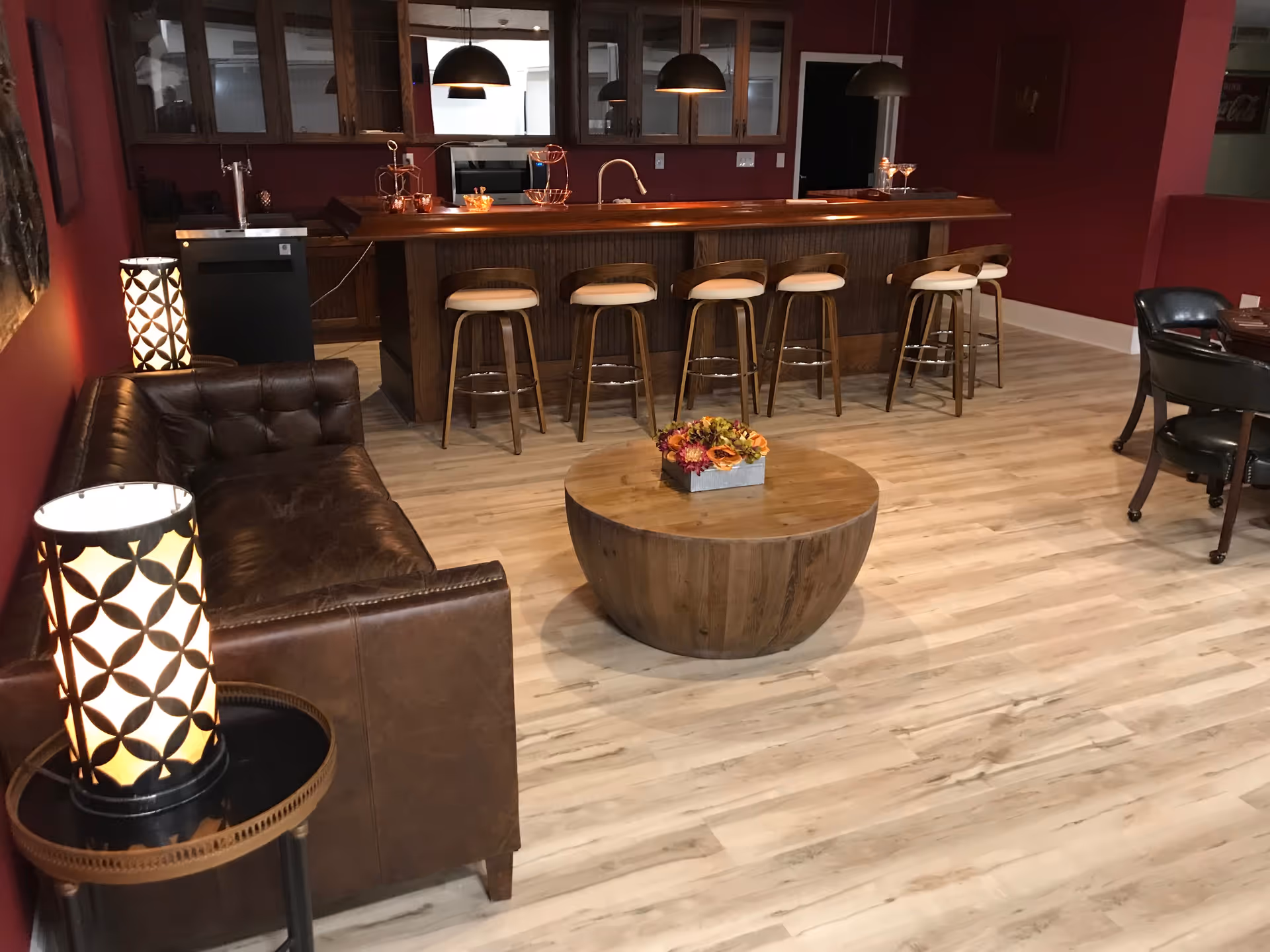 Cozy lounge area with a leather sofa, round wooden coffee table with flowers, and a bar counter with stools under pendant lights.