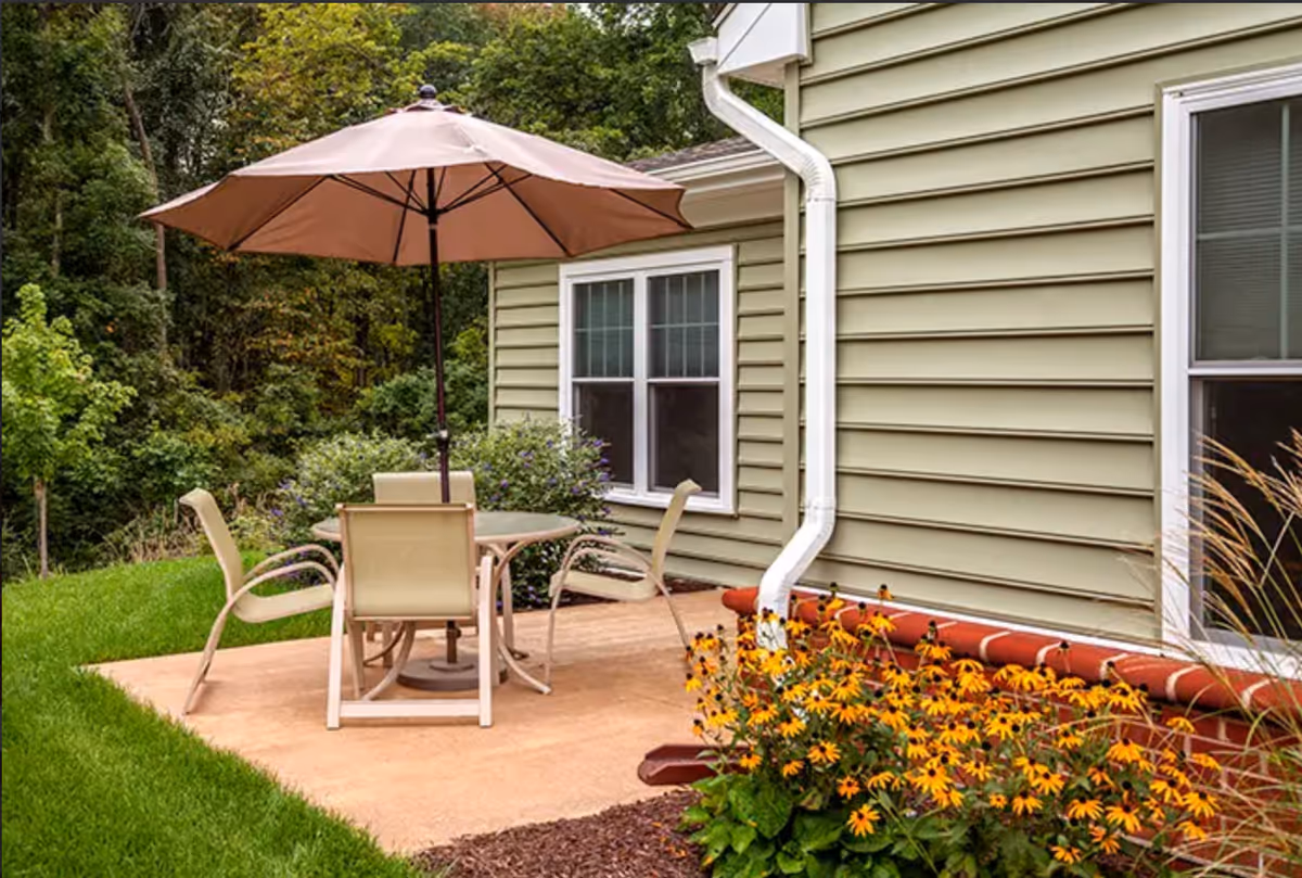 Outdoor patio with a round table, chairs, and umbrella beside a beige house.